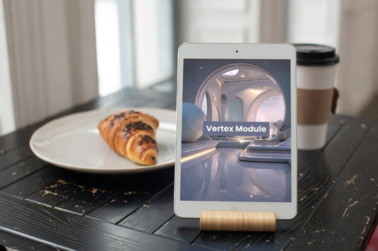 Tablet on a stand displaying 'Vertex Module' course, next to a croissant and coffee cup on a wooden table.