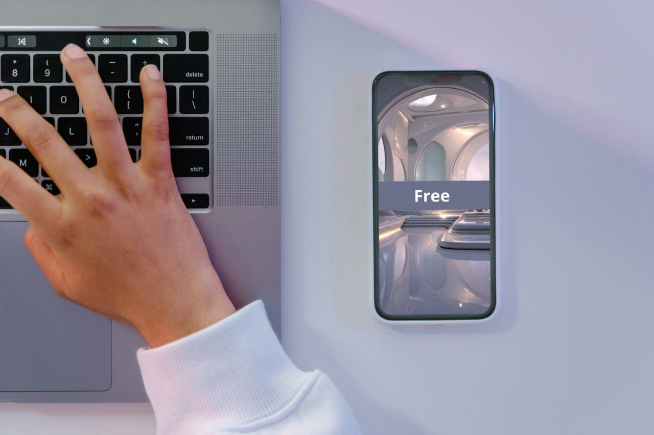Person using a laptop with a smartphone showing an 3D modeling course cover named 'Free'.