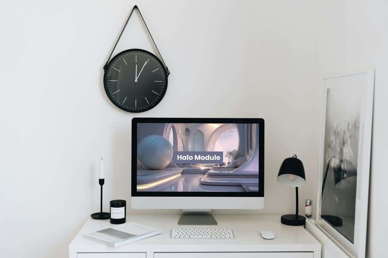 Modern office setup with computer monitor, clock, and decor on a white wall.