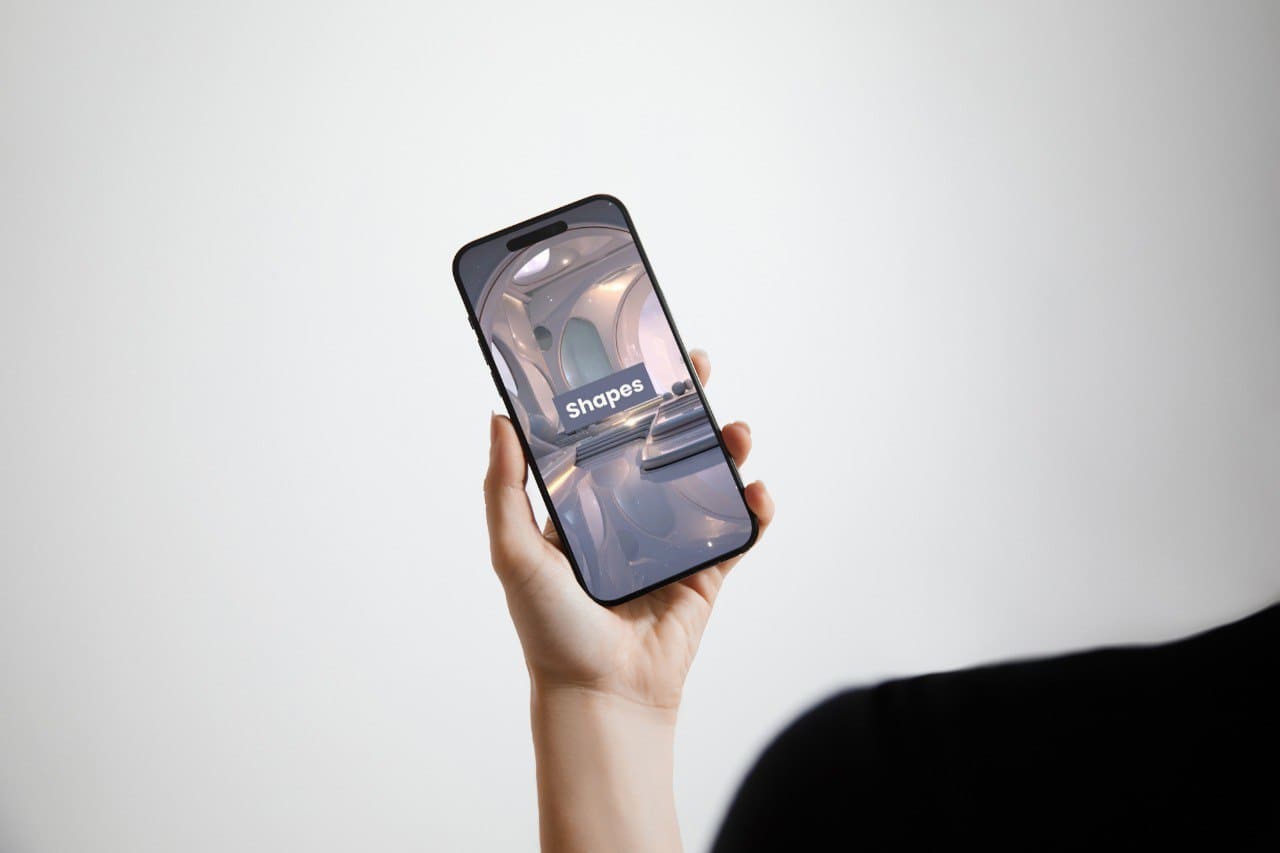 Hand holding a smartphone with a 'Shapes' course interface on a light gray background